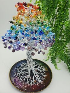 a glass tree with many different colored stones on it's branches and roots, sitting next to a fern