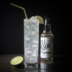 a glass filled with ice and lime next to a bottle