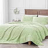 a bed with green bedspread and pillows in a white room next to a wooden headboard