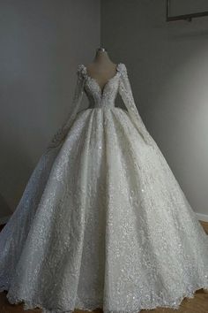 a white wedding dress with long sleeves on display in front of a light fixture and wooden floor