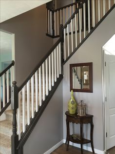 an entryway with stairs, mirror and vase on the table in front of it