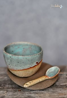 a small blue bowl and spoon sitting on top of a wooden table next to each other