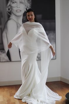 a woman standing in front of a painting wearing a long white dress with sheer sleeves