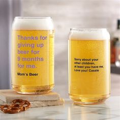 two beer glasses sitting on top of a counter next to a pretzel and bottle