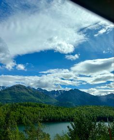 a scenic view of mountains, trees and water from a train window with the sky in the background