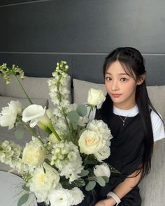 a woman sitting on a couch holding a bouquet of white flowers and greenery in front of her