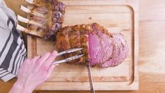 a person cutting meat on top of a wooden cutting board next to a knife and fork