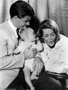 a man and woman holding a baby in their lap while looking at something on the table