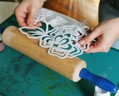 a person is cutting out paper with a rolling pin on a green surface and blue handles