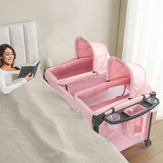 a woman sitting on a bed reading a book next to a baby crib and changing table