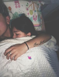 two people laying in bed with one holding the other's head and hugging each other