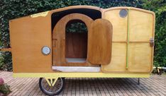 an old fashioned yellow trailer is parked in front of some bushes