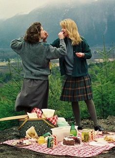 two people standing on top of a picnic table with food and drinks in front of them