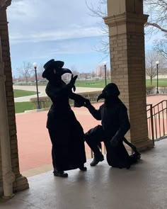 two people dressed in black standing next to each other on a porch with columns and pillars