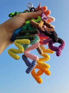 there is a hand holding several crocheted objects in the air with blue sky behind it