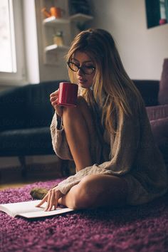 a woman sitting on the floor holding a red coffee cup and looking at her laptop