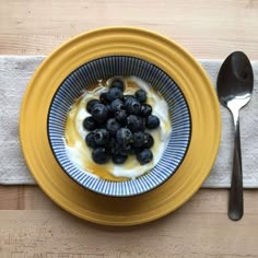 a yellow plate topped with blueberries and yogurt next to a silver spoon