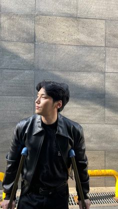 a man in black leather jacket standing next to a wall