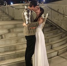 a man and woman dressed in knight costumes kissing on the steps with their arms around each other