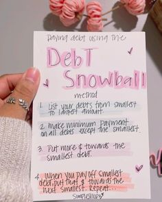 a person holding up a paper with writing on it that says debt snowball and two balls of yarn in the background