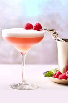 raspberry martini in a coupe glass with fresh raspberries on the rim