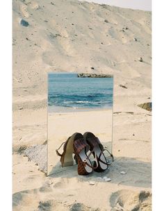 a pair of shoes sitting on top of a sandy beach next to a large mirror