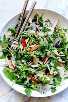 a white bowl filled with salad on top of a marble counter topped with wooden utensils