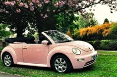 a pink convertible car parked in front of a tree