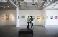 two people standing in an art gallery looking at paintings