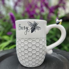 a white coffee cup with a bee on it and the words busy written in black