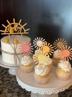 cupcakes with white frosting and sunburst decorations on top of a cake stand