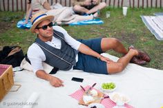 a man sitting on top of a white table next to a picnic basket filled with food