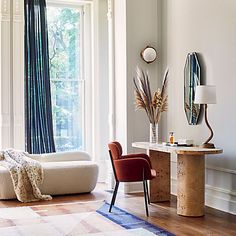 a living room filled with furniture next to a large window and a rug on top of a hard wood floor