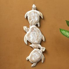 three carved turtles sitting next to each other on a brown surface with green plants in the background