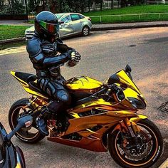 a man in black and yellow leathers riding a motorcycle on the street next to parked cars