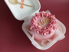 a heart shaped cake with the word love on it in a box next to a spoon