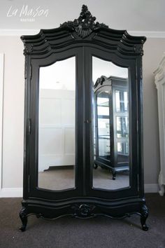 an ornate black armoire with mirrored doors and mirror on the front, sitting in a room