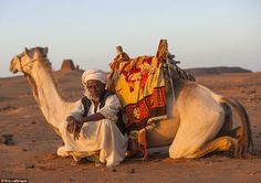 a man sitting next to a camel in the desert