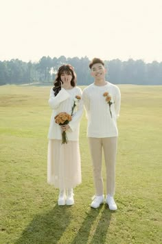 two people standing in the grass with flowers