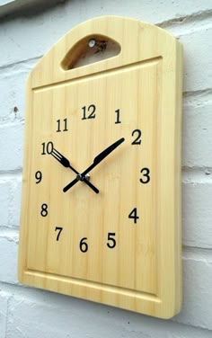 a wooden clock mounted to the side of a white brick wall with numbers on it