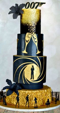 a black and gold cake with golden decorations on the top, surrounded by figurines