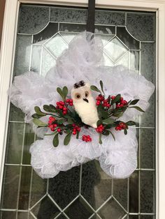 a white wreath with an owl and red berries hanging on the front door glass window