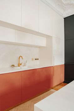 a kitchen with red cabinets and white counter tops, gold faucet in the middle