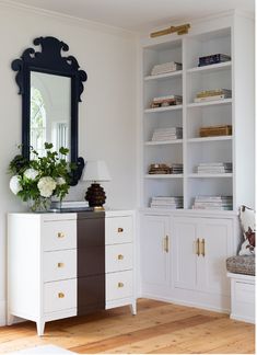 a room with white cabinets and a mirror on the wall next to a vase filled with flowers