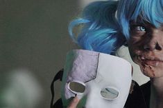 a woman with blue hair holding up a mask