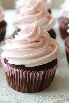 cupcakes with pink frosting sitting on top of a white doily covered table