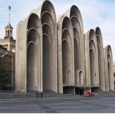 a large building with arches on the side and a red car parked in front of it