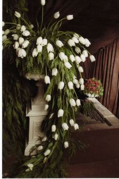 white flowers and greenery are hanging from a pillar in front of a wooden wall