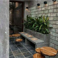 an outdoor seating area with tables and stools in front of a brick wall that has plants growing on it