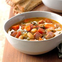 a white bowl filled with soup next to a slice of bread on top of a cutting board